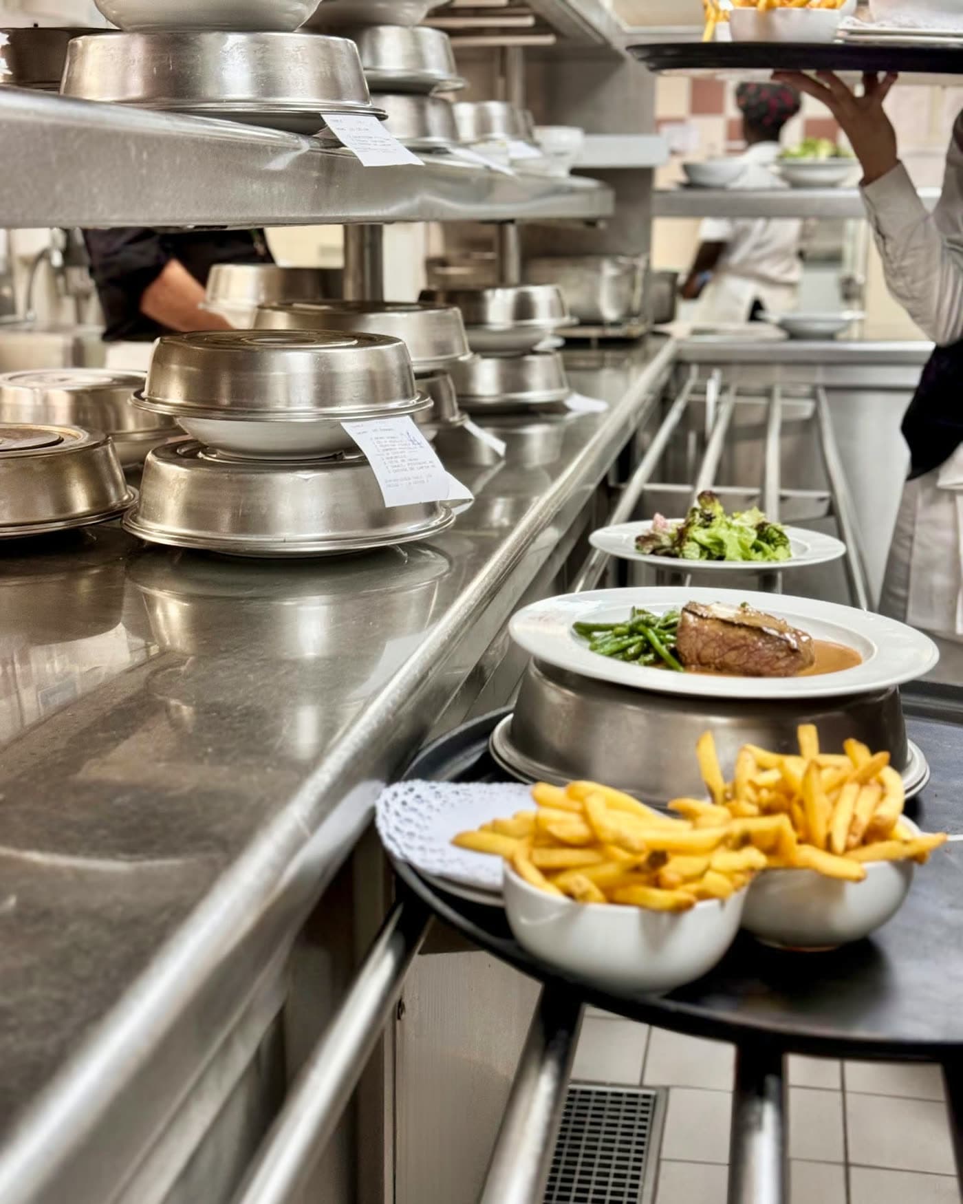 Passe de cuisine avec cloches inox, frites et plat en sauce prêts à servir — Brasserie Georges