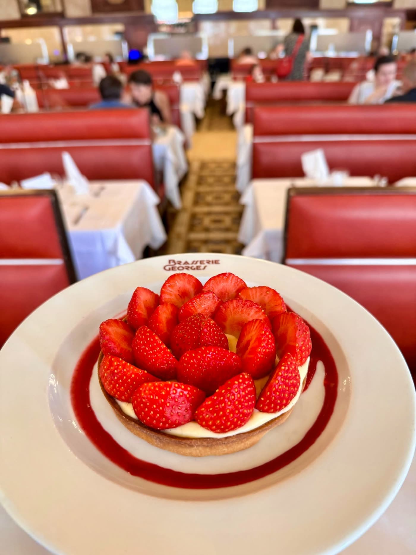 Tarte aux fraises sur assiette siglée, banquettes rouges en arrière-plan flou — Brasserie Georges