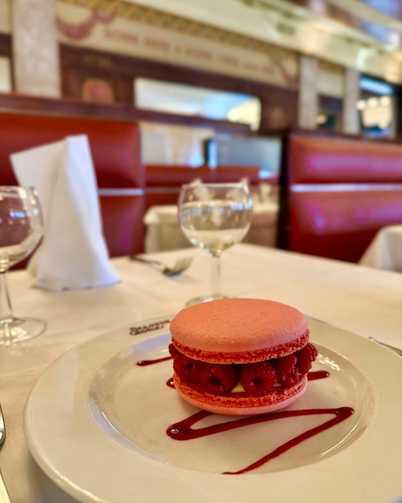Macaron géant framboise sur assiette siglée, verres à vin en bokeh — Brasserie Georges