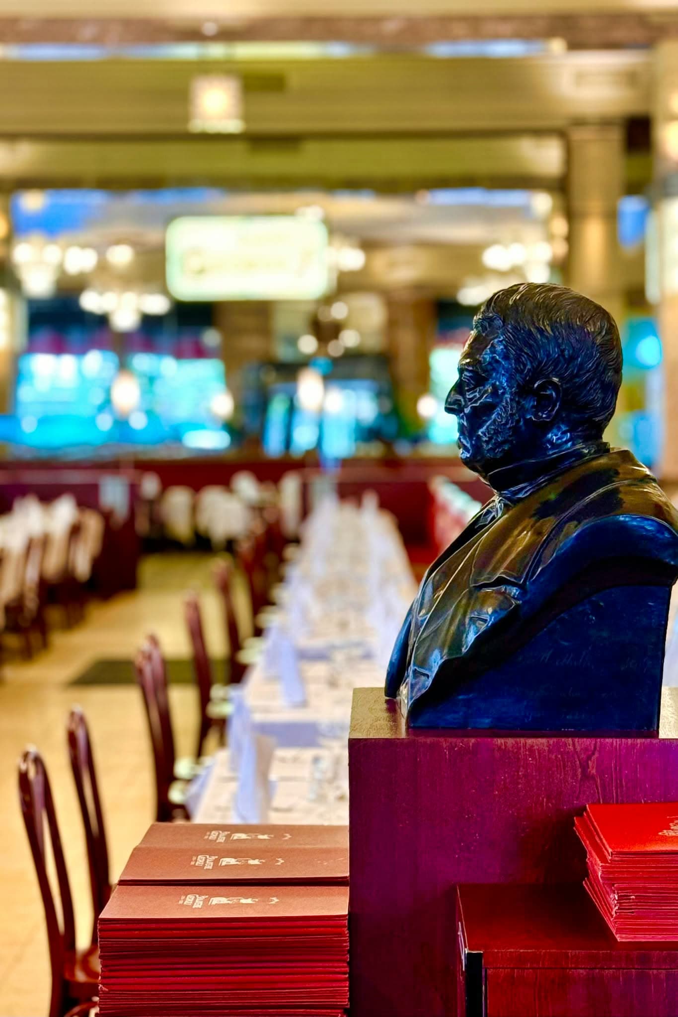 Buste du fondateur dans une ambiance sombre, salle et menus rouges en arrière-plan — Brasserie Georges