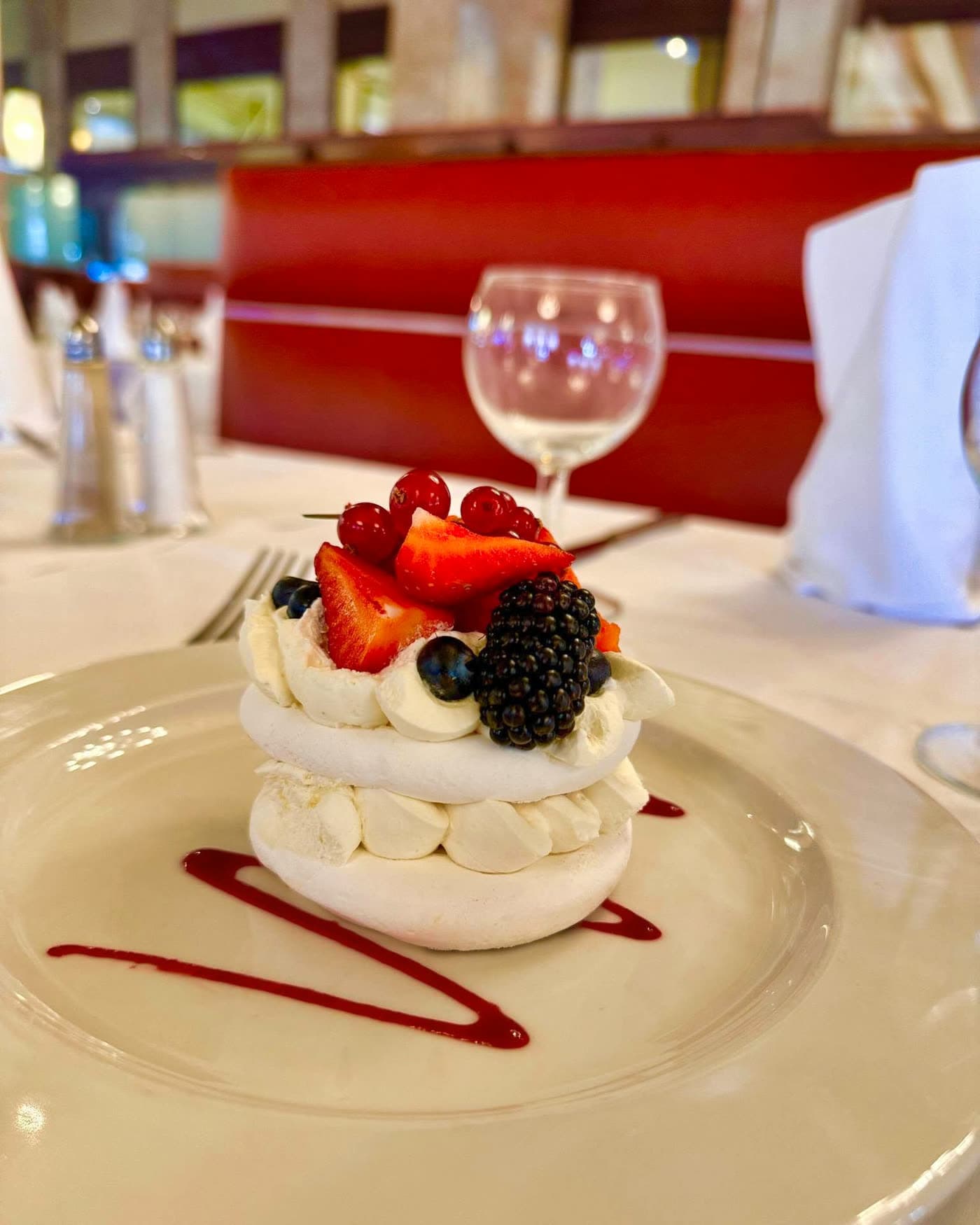 Pavlova meringuée garnie de fruits rouges sur assiette blanche, banquette rouge en fond — Brasserie Georges