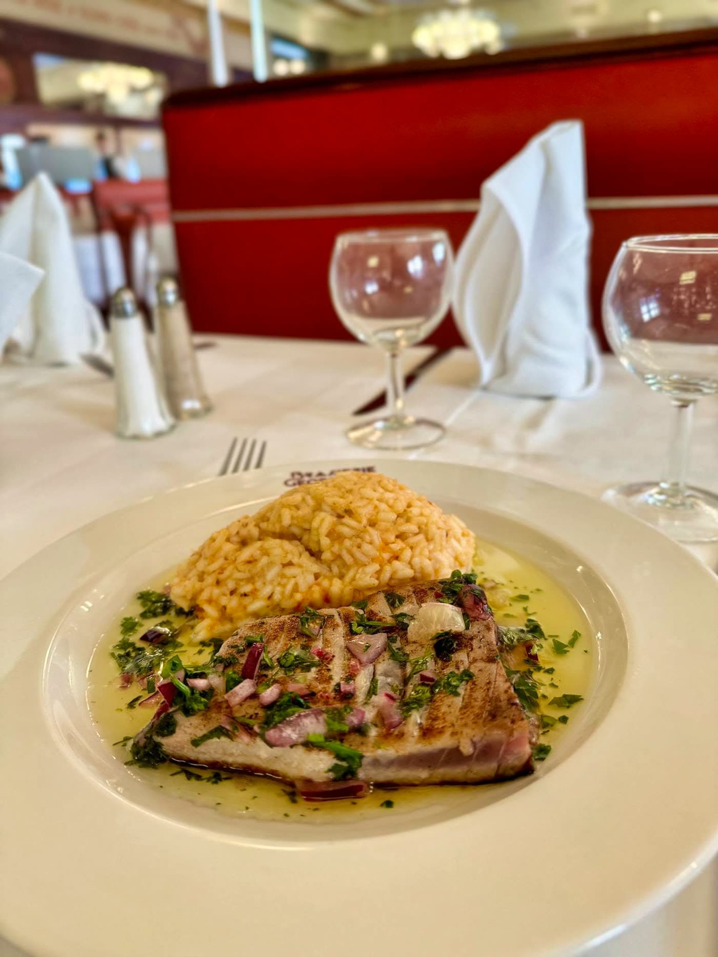 Filet de poisson grillé aux herbes avec riz, verres à vin et banquette rouge en fond — Brasserie Georges