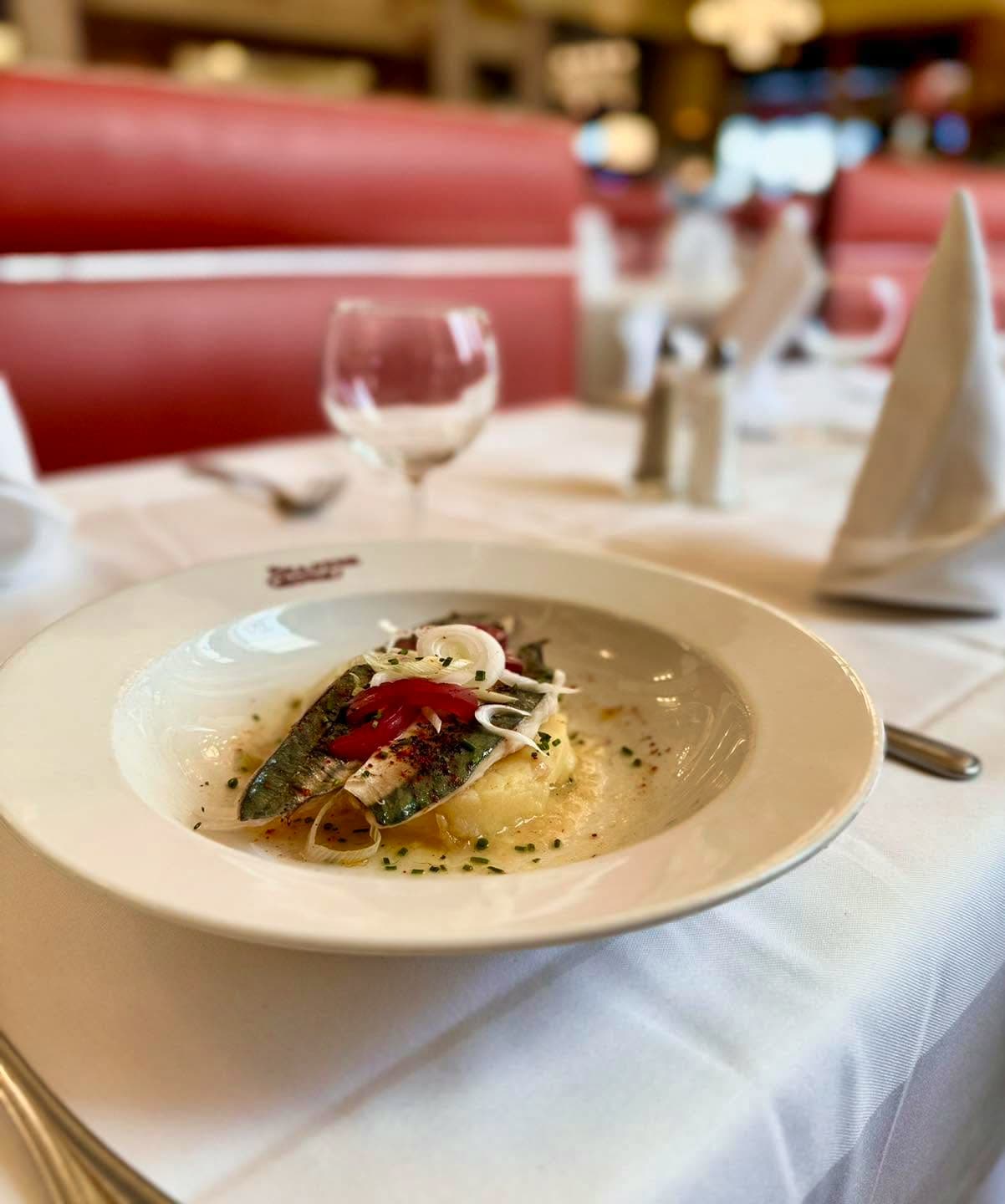 Assiette de poisson mariné avec agrumes et sauce, table dressée, banquette rouge floutée — Brasserie Georges