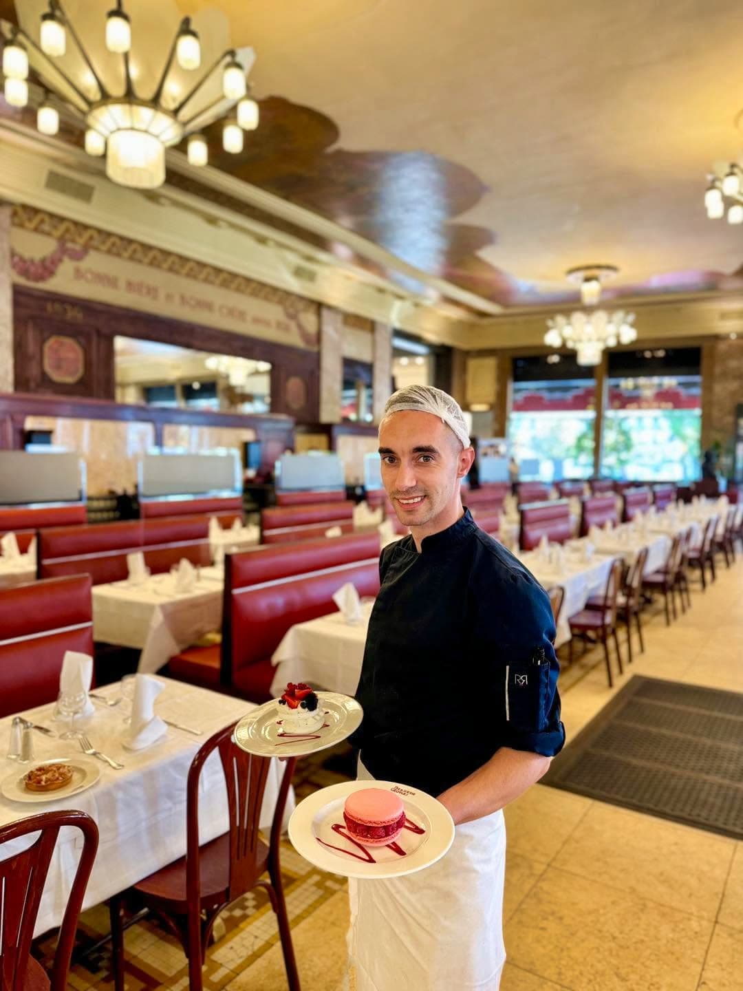 Serveur souriant portant deux assiettes de dessert dans la grande salle — Brasserie Georges
