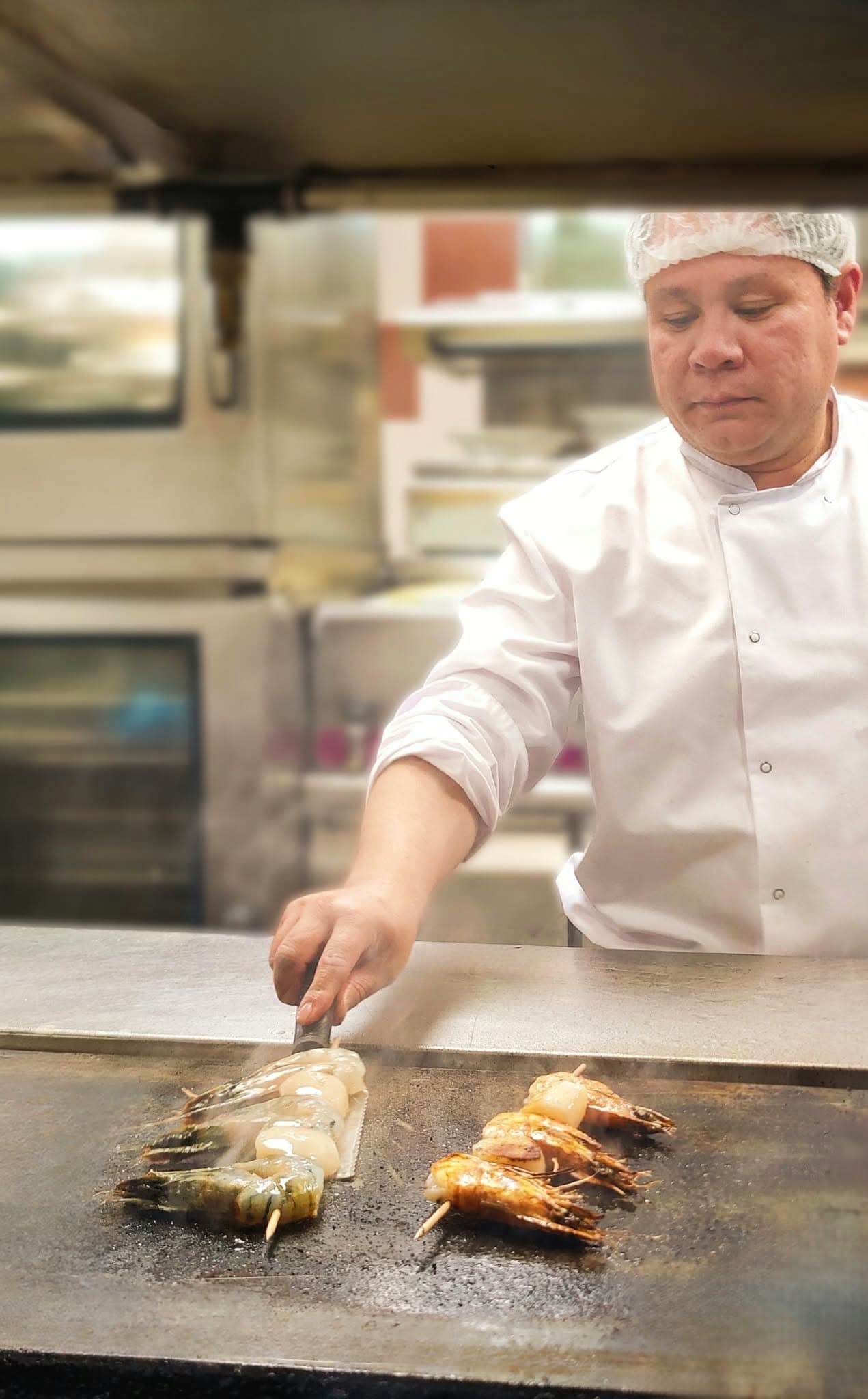 Cuisinier grillant des brochettes de gambas sur plancha en cuisine — Brasserie Georges