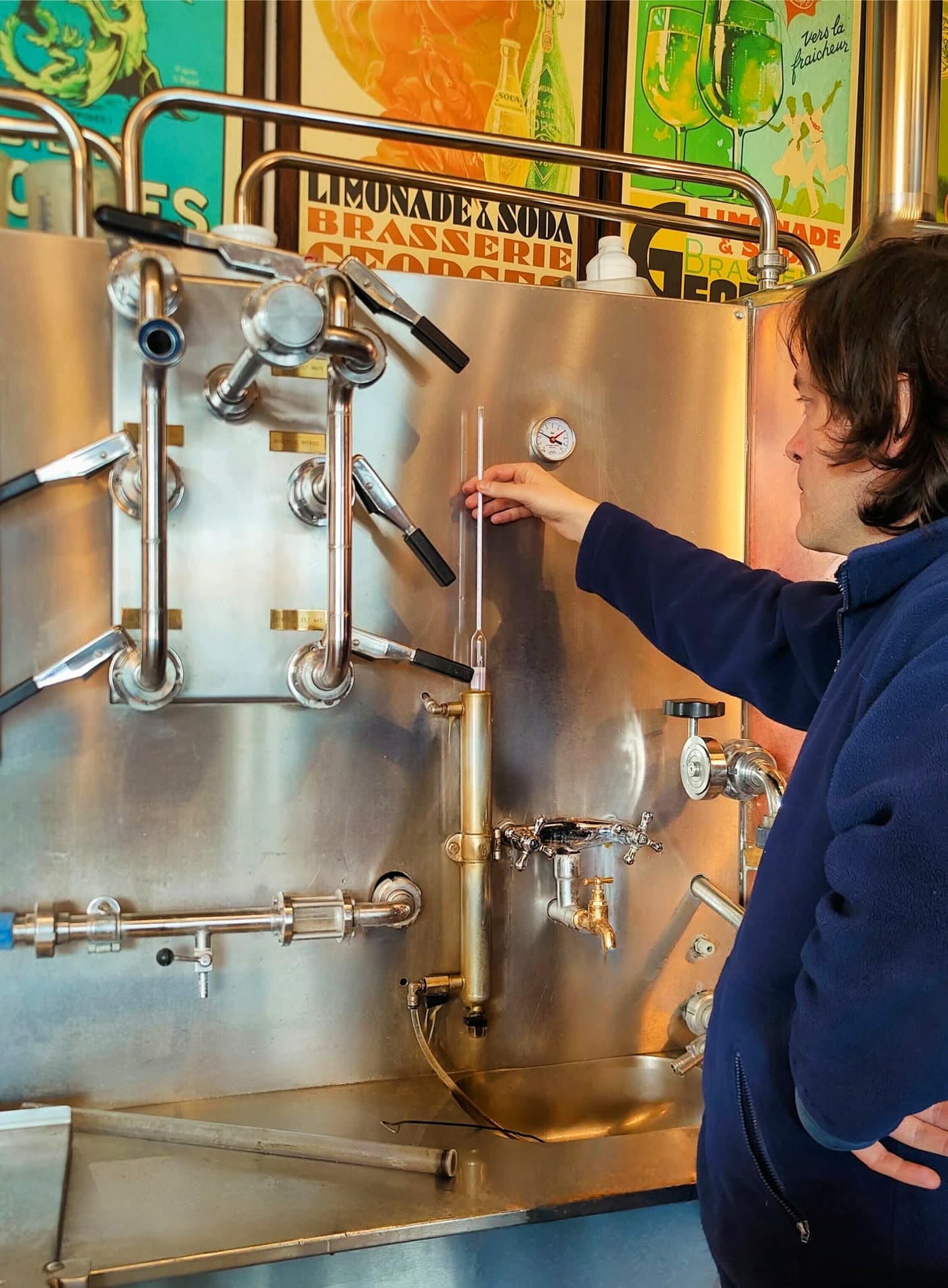 Personne réglant une jauge sur une cuve de brassage en inox, affiches en fond — Brasserie Georges