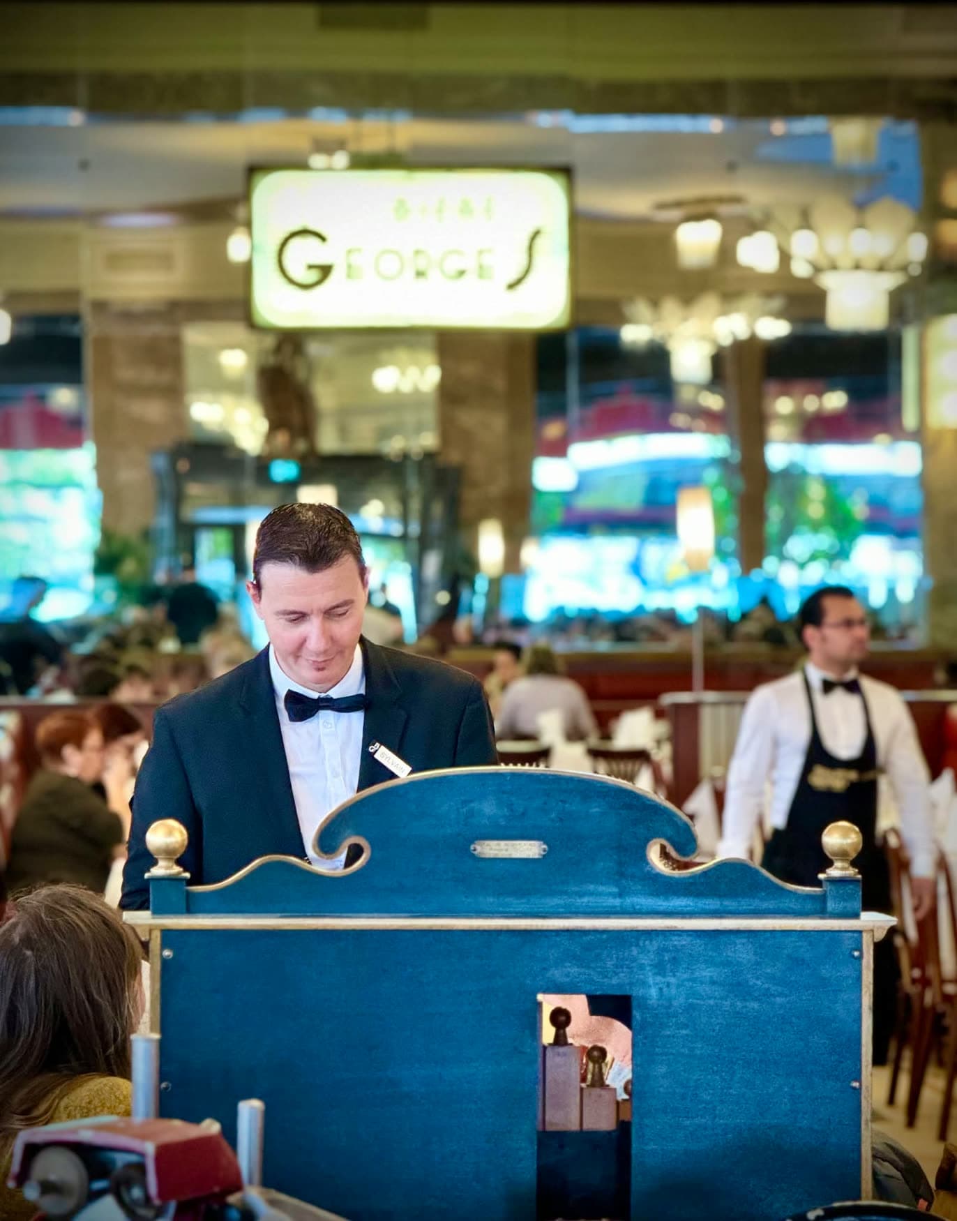 Pianiste en costume jouant du piano dans la salle, enseigne « Bières Georges » lumineuse en fond — Brasserie Georges