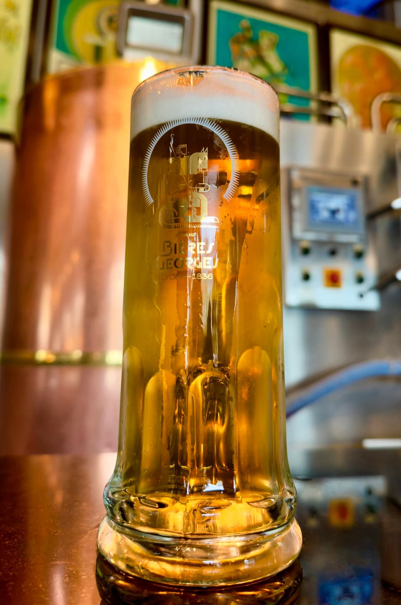 Chope de bière blonde Bières Georges au comptoir, cuivre et affiches en fond flou — Brasserie Georges