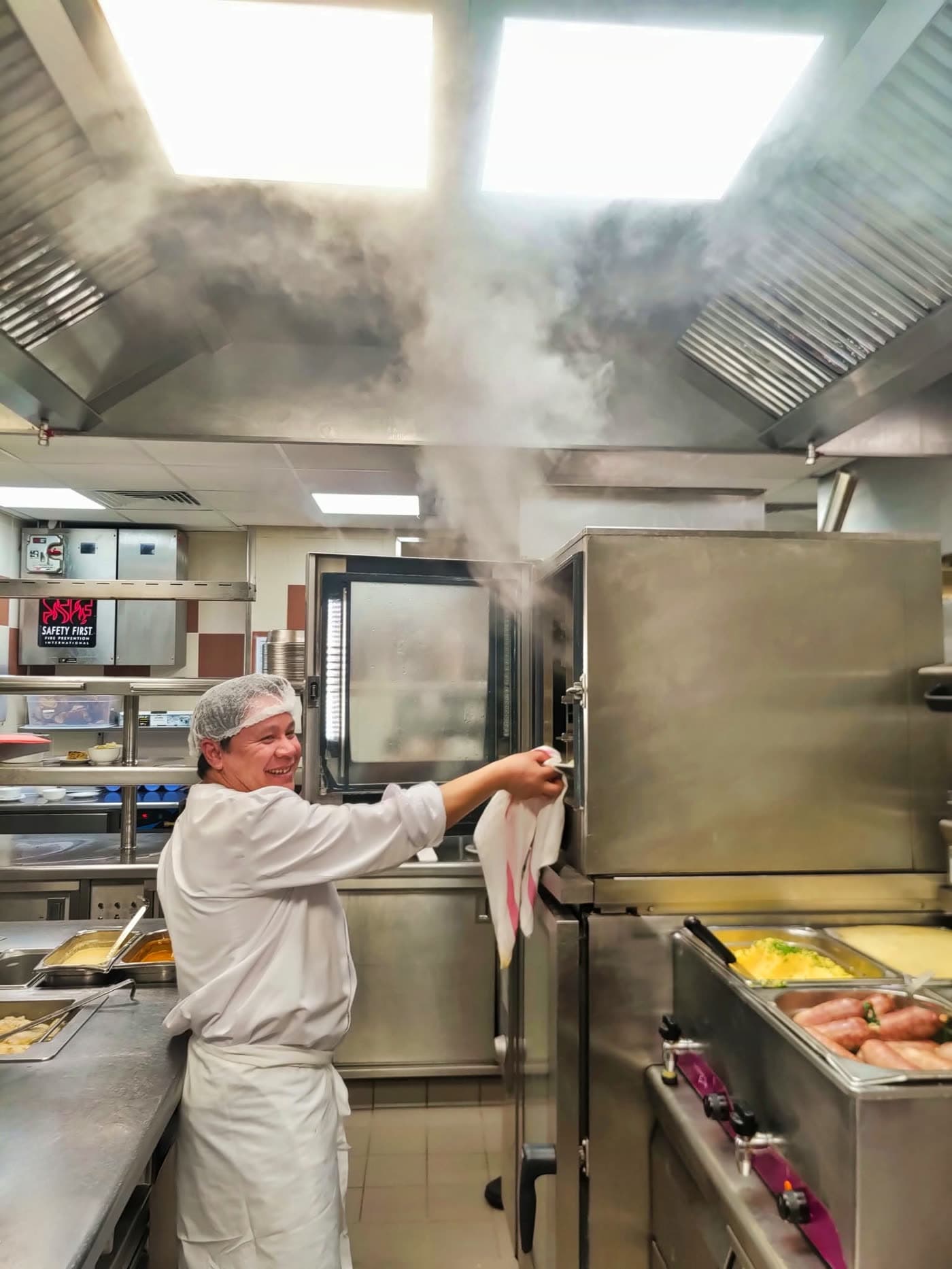 Cuisinier en veste blanche ouvre un four à vapeur, fumée s'échappant sous verrières — Brasserie Georges