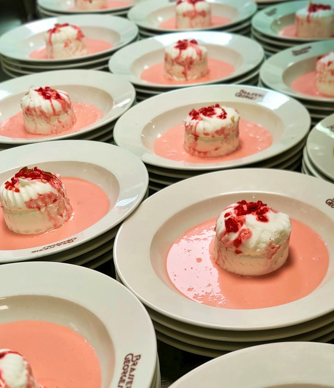 Série de desserts identiques, mousse blanche sur coulis rose, préparation en cuisine pour banquet — Brasserie Georges