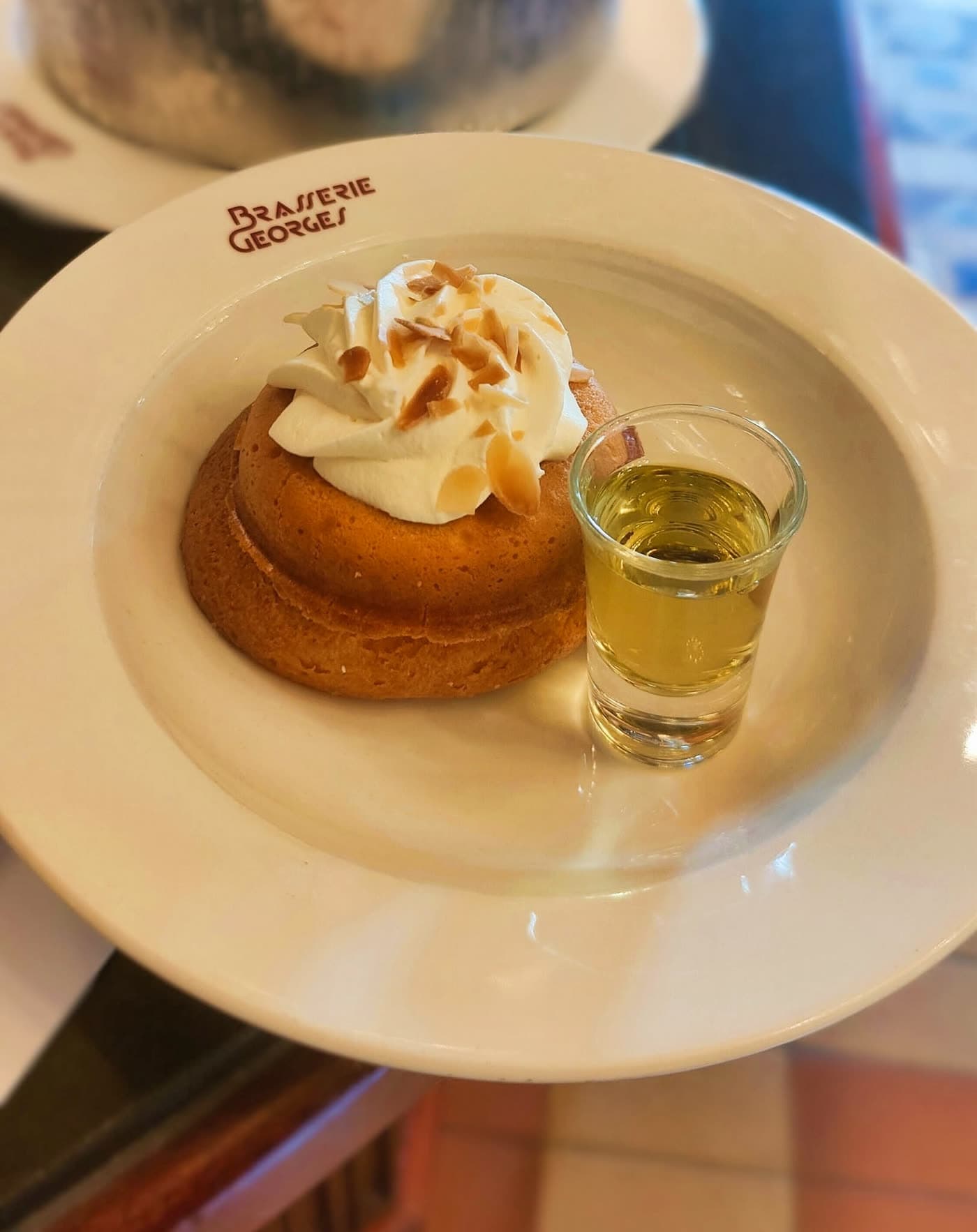 Baba imbibé nappé de chantilly avec mignonnette d'alcool, assiette marquée Brasserie Georges