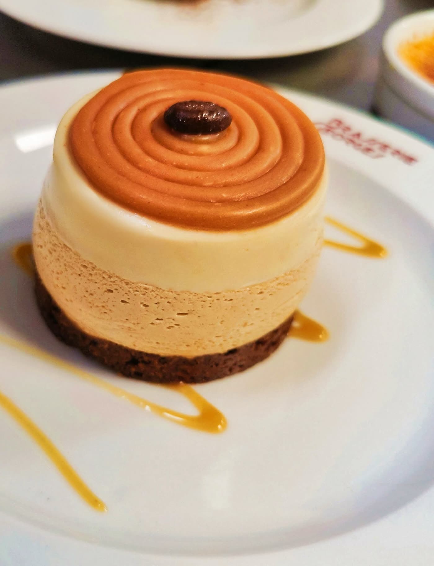 Entremets rond caramel-café avec grain de café en décor et traits de caramel sur assiette — Brasserie Georges