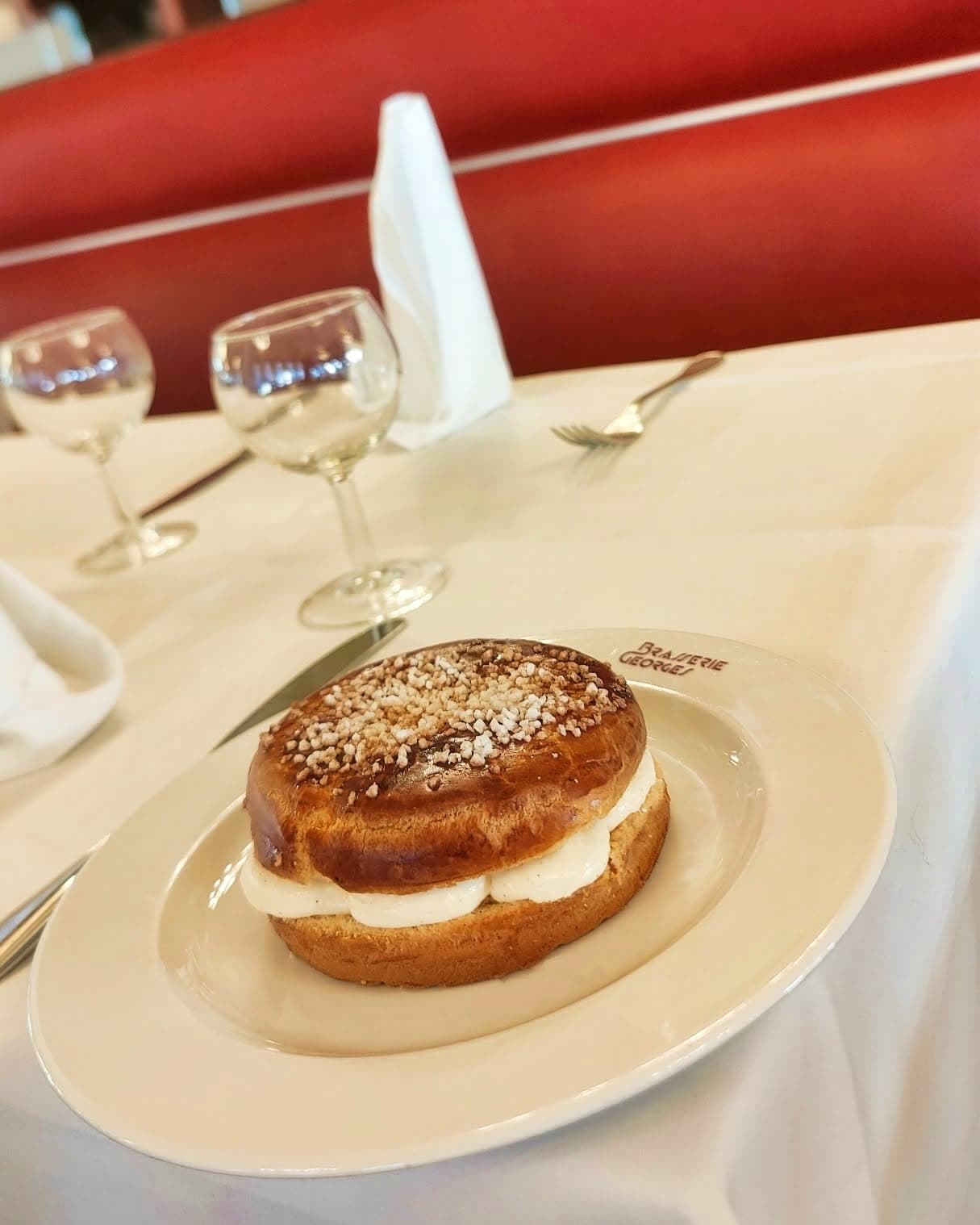 Brioche garnie de crème façon tropézienne posée sur nappe blanche, verres à vin en arrière-plan — Brasserie Georges