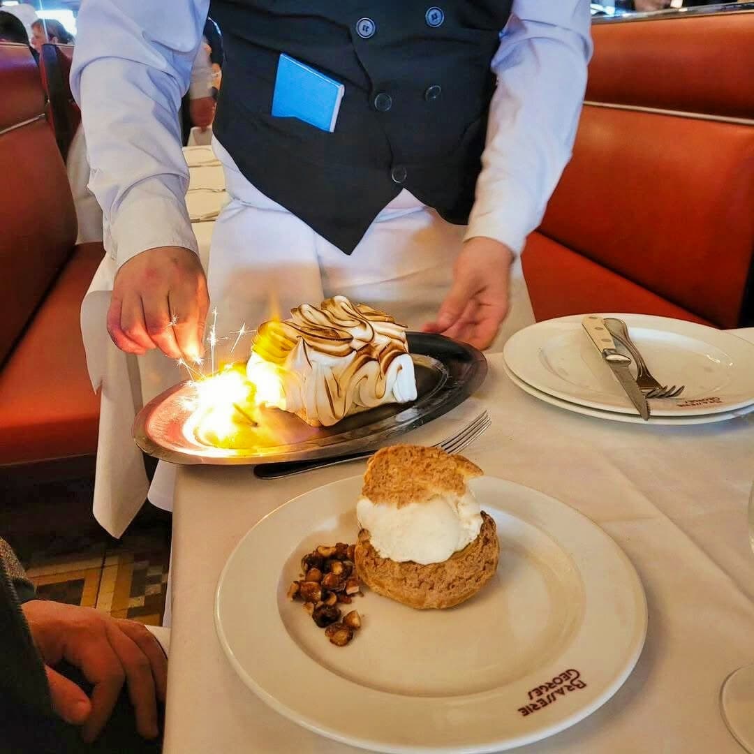 Serveur flambe une omelette norvégienne avec bougies devant une assiette de chou à la crème — Brasserie Georges