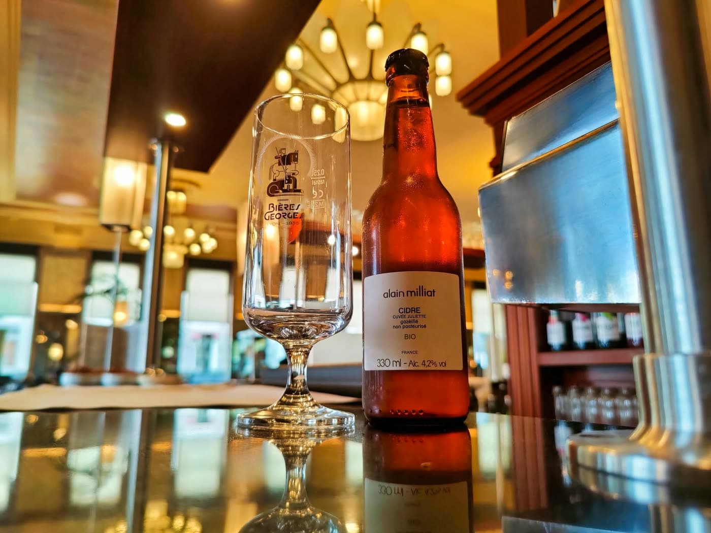 Verre Brasserie Georges vide posé à côté d'une bouteille de bière artisanale sur le comptoir du bar