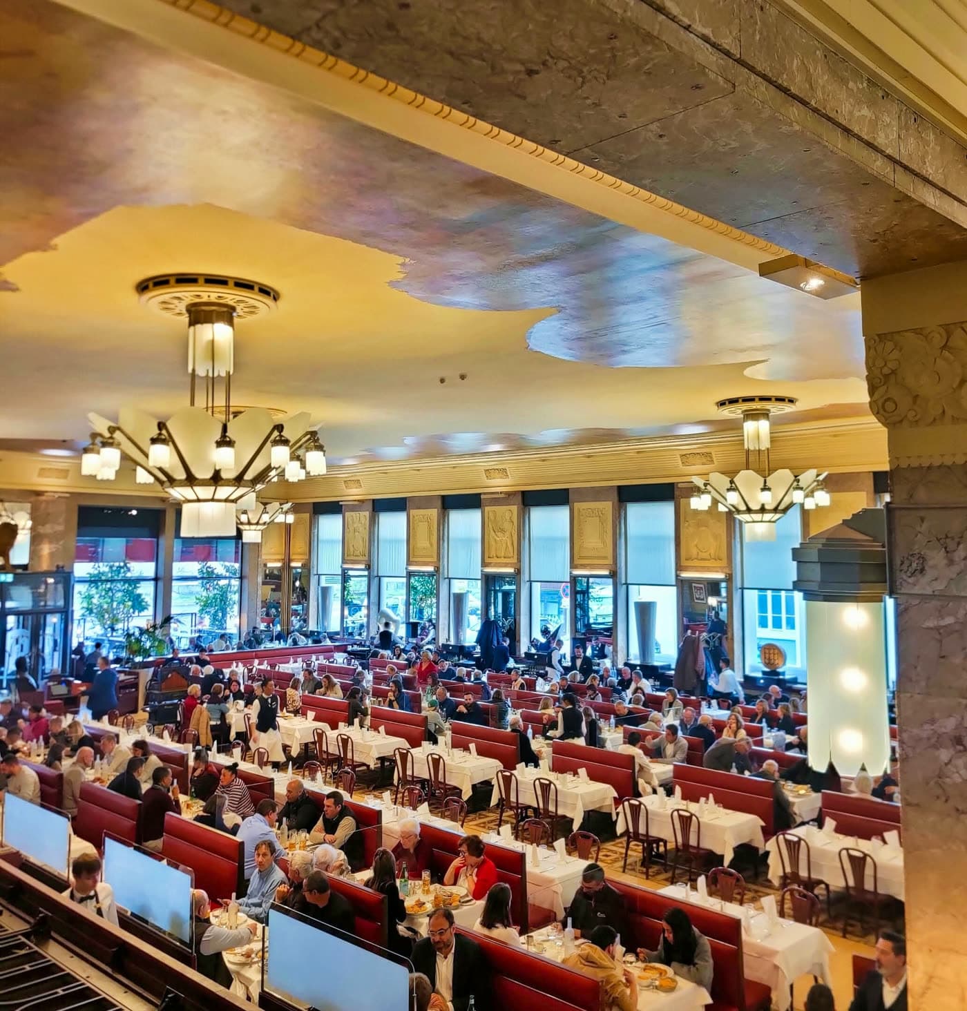 Vue en hauteur de la grande salle Art déco avec lustres et tables pleines de clients — Brasserie Georges
