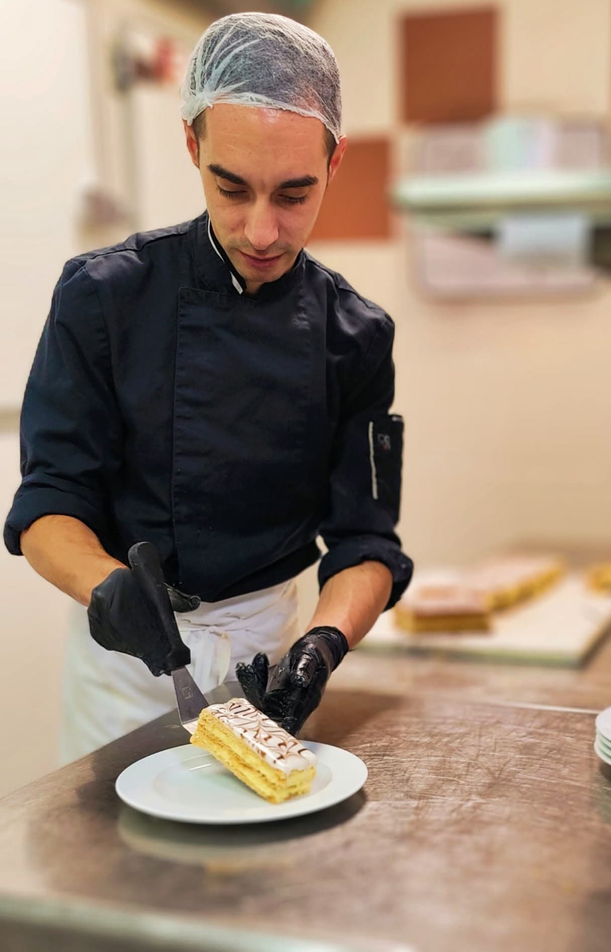 Pâtissier en cuisine dresse un mille-feuille au couteau, charlotte filet en réserve à l'arrière-plan — Brasserie Georges