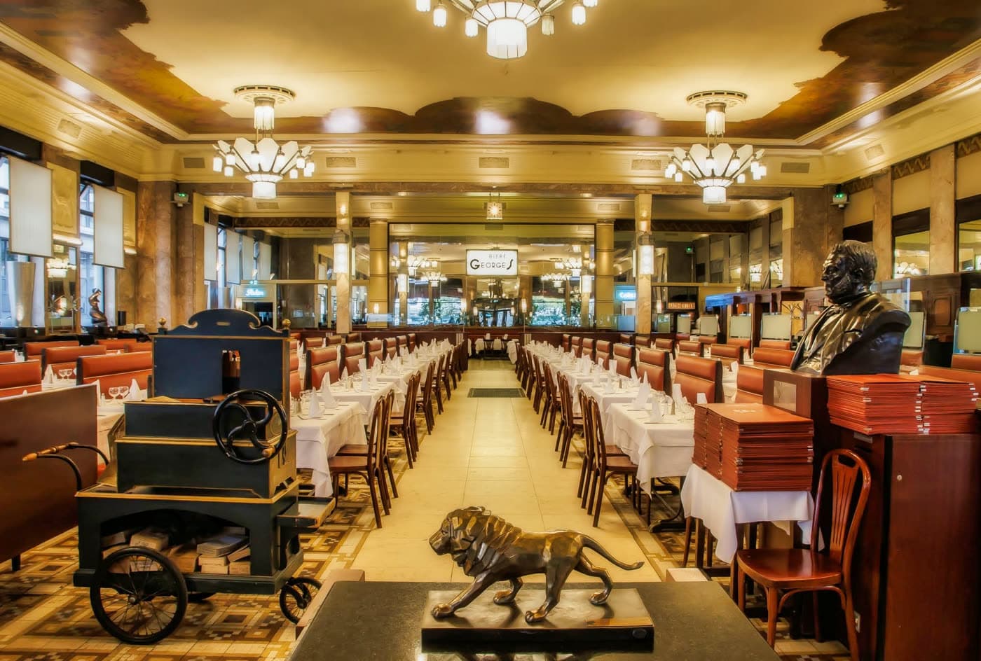 Grande salle Art déco, chariot de service noir, lion en bronze, buste, tables dressées — Brasserie Georges