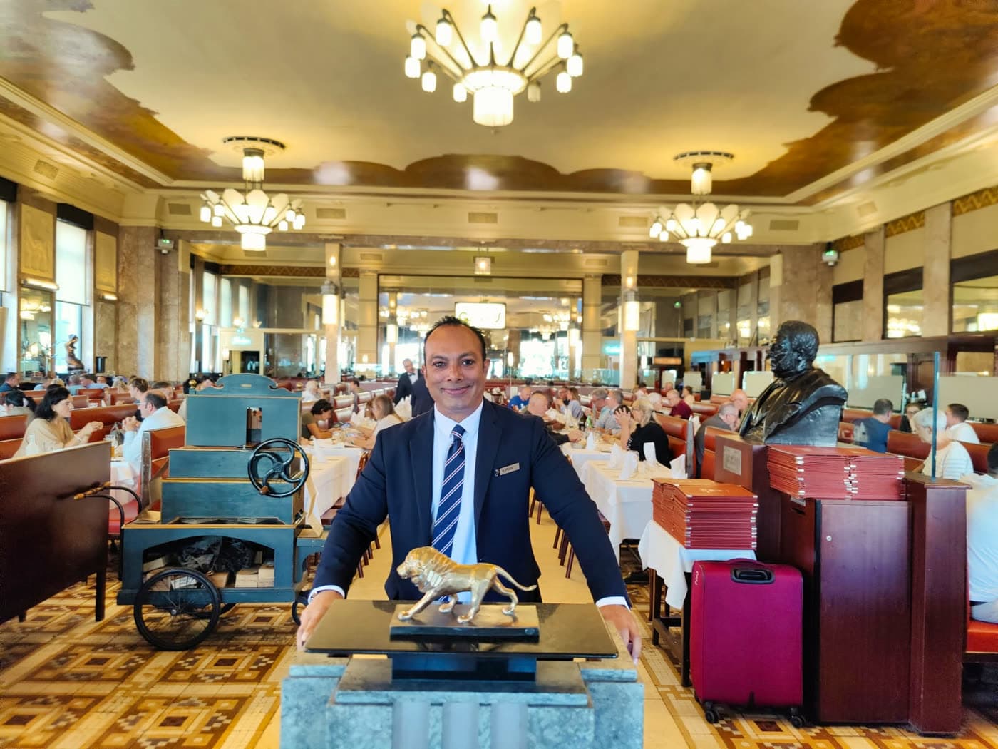 Homme en costume dans la salle, statue de lion en bronze, décor vintage, salle pleine — Brasserie Georges