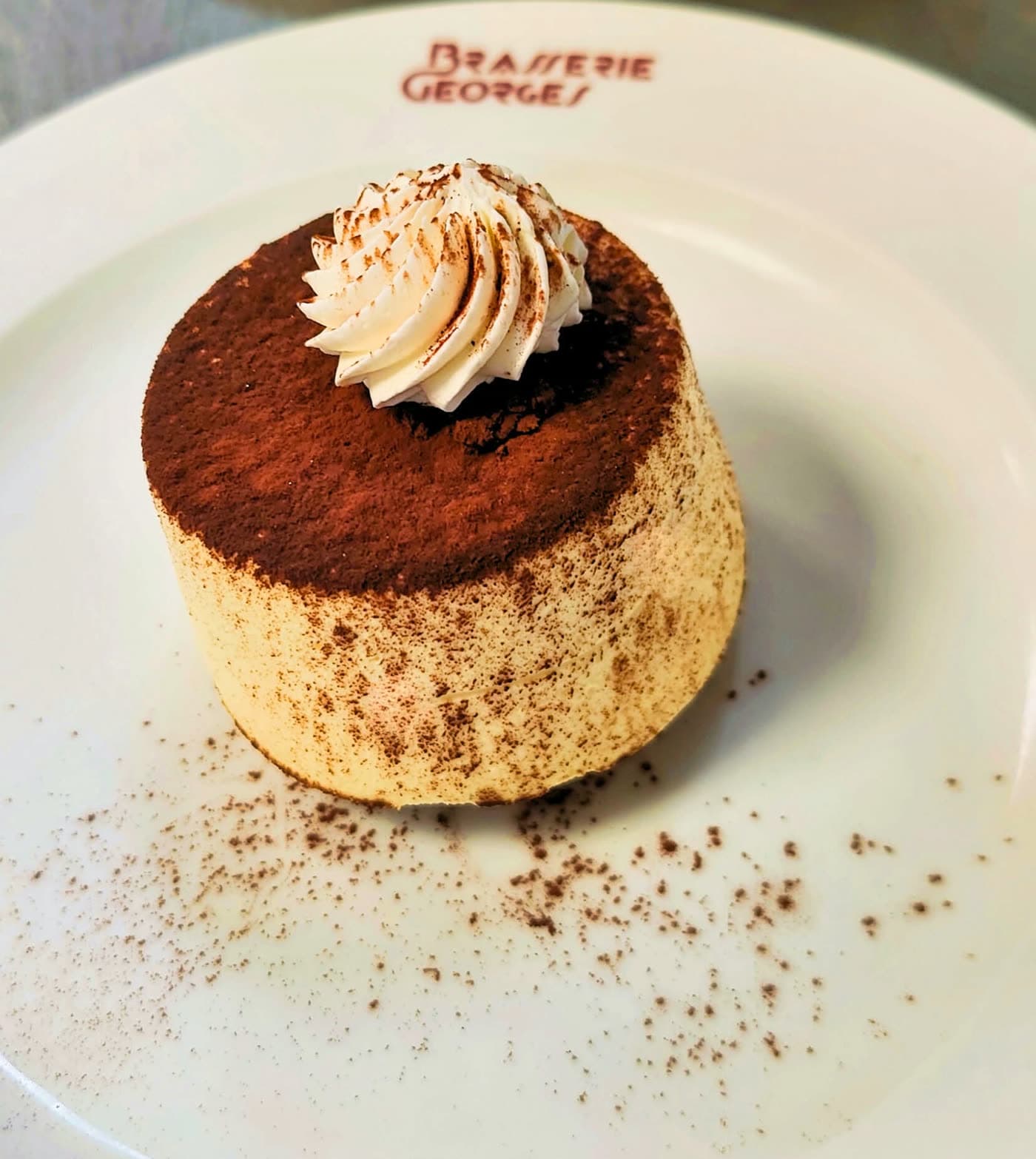 Petit gâteau rond cacao et chantilly sur assiette logotée Brasserie Georges