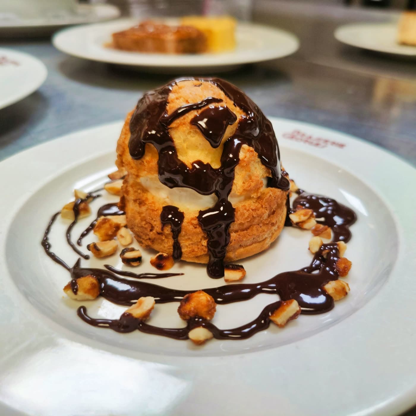 Chou pâtissier nappé de chocolat et éclats de noisettes sur assiette logotée — Brasserie Georges