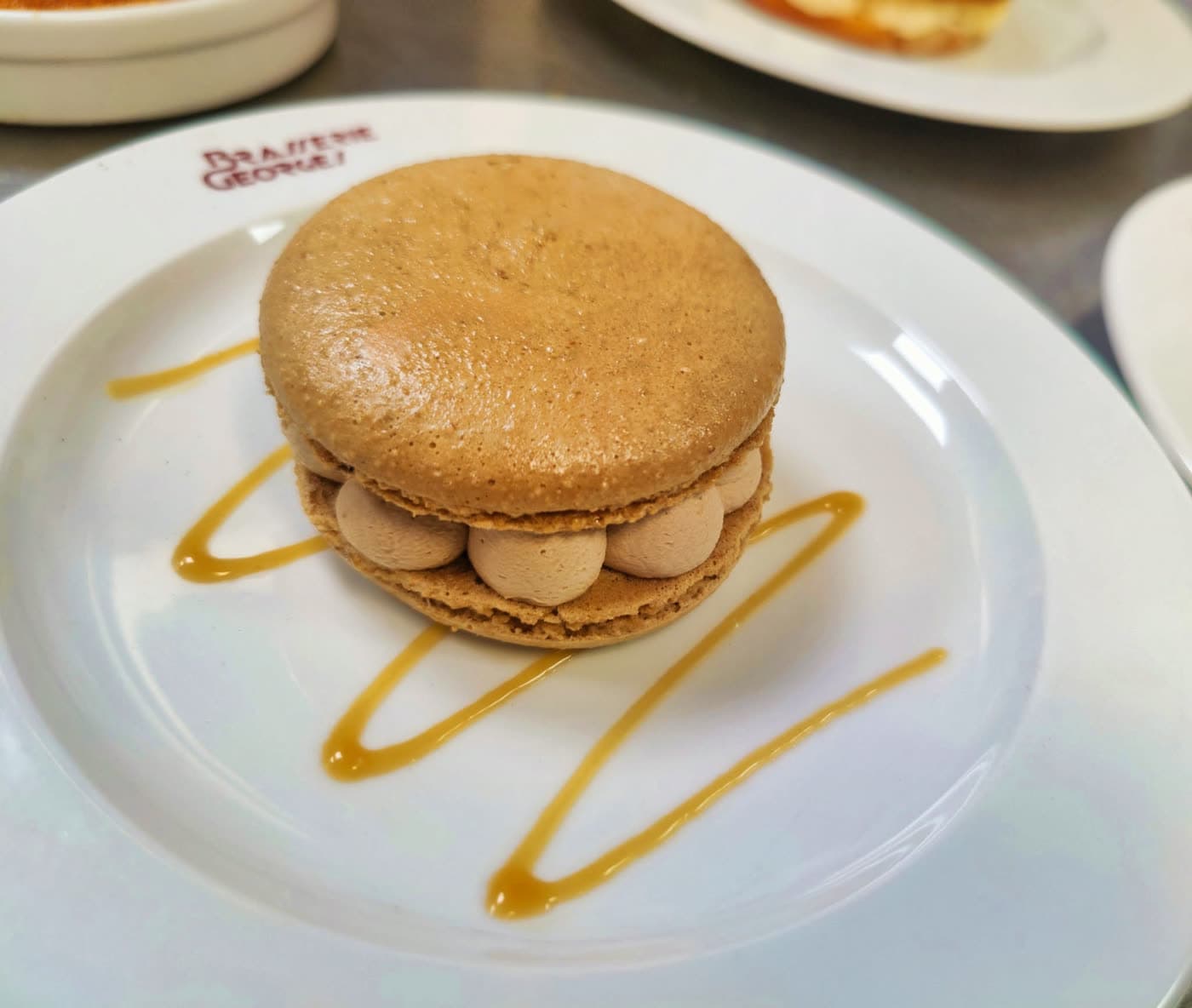 Gros macaron caramel avec filet de sauce caramel sur assiette logotée — Brasserie Georges