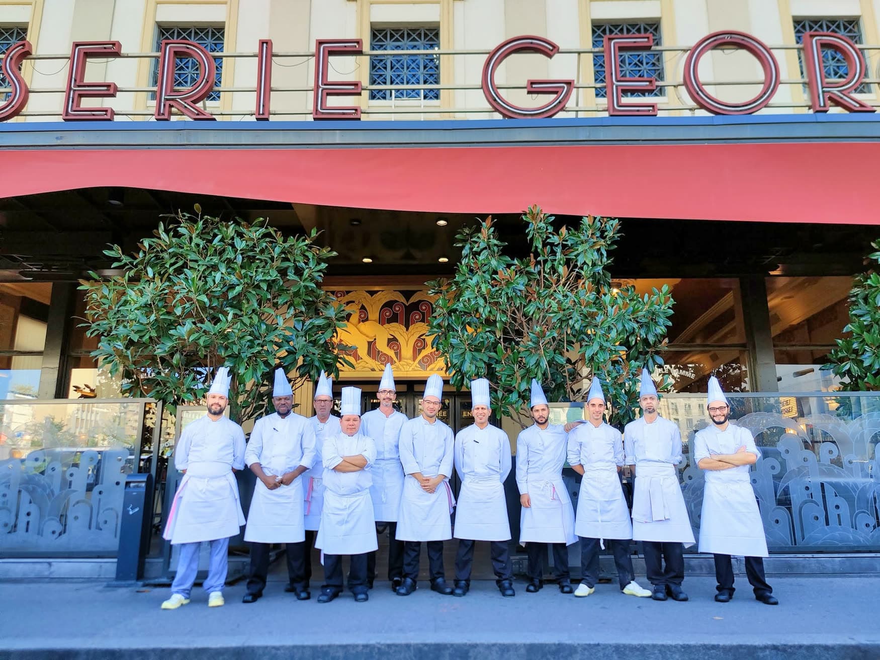 Brigade de cuisine alignée en toque blanche sous l'auvent rouge de la façade — Brasserie Georges