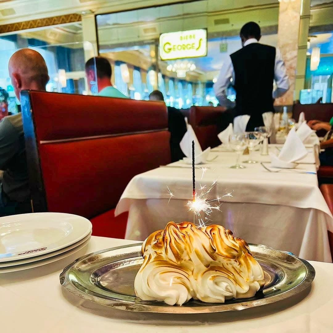 Omelette norvégienne flambée avec cierge magique sur plateau argenté, salle en fond — Brasserie Georges