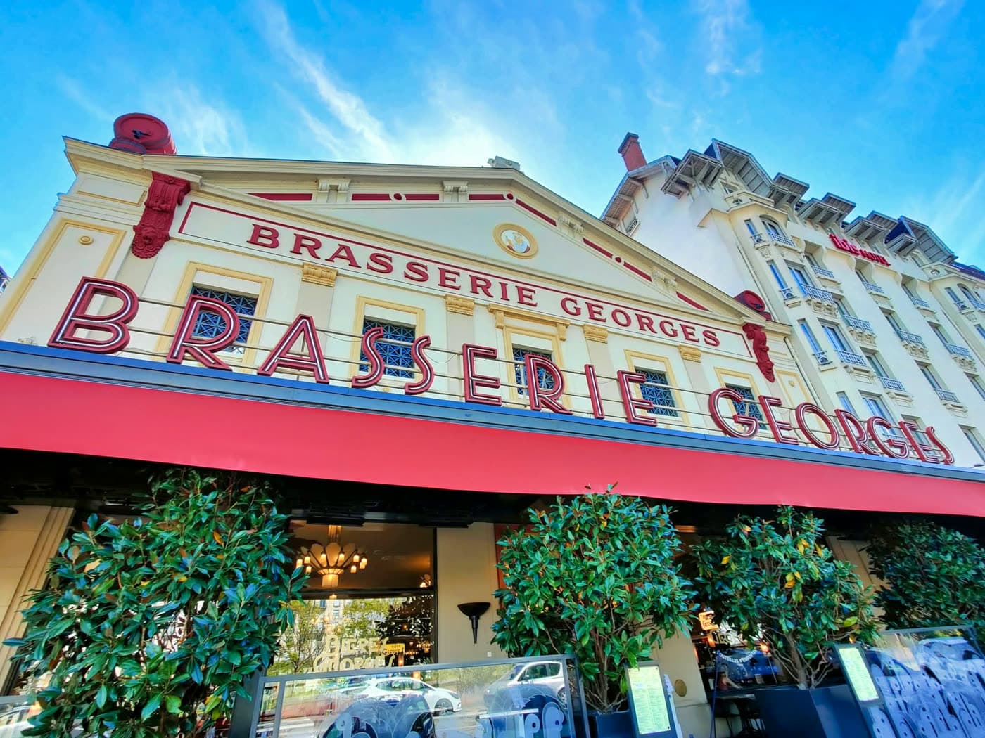 Façade jaune et rouge de la brasserie de jour, enseignes et jardinières devant l'entrée — Brasserie Georges