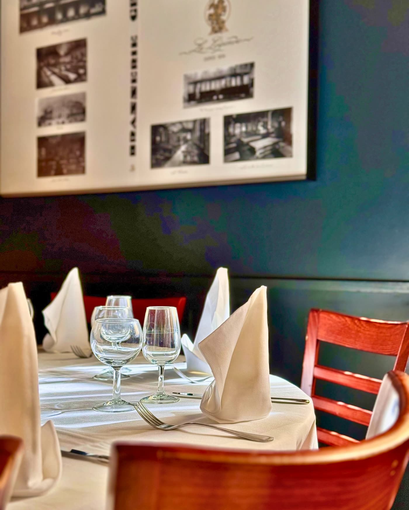 Table dressée avec verres et serviettes pliées devant mur bleu et photos anciennes — Brasserie Georges
