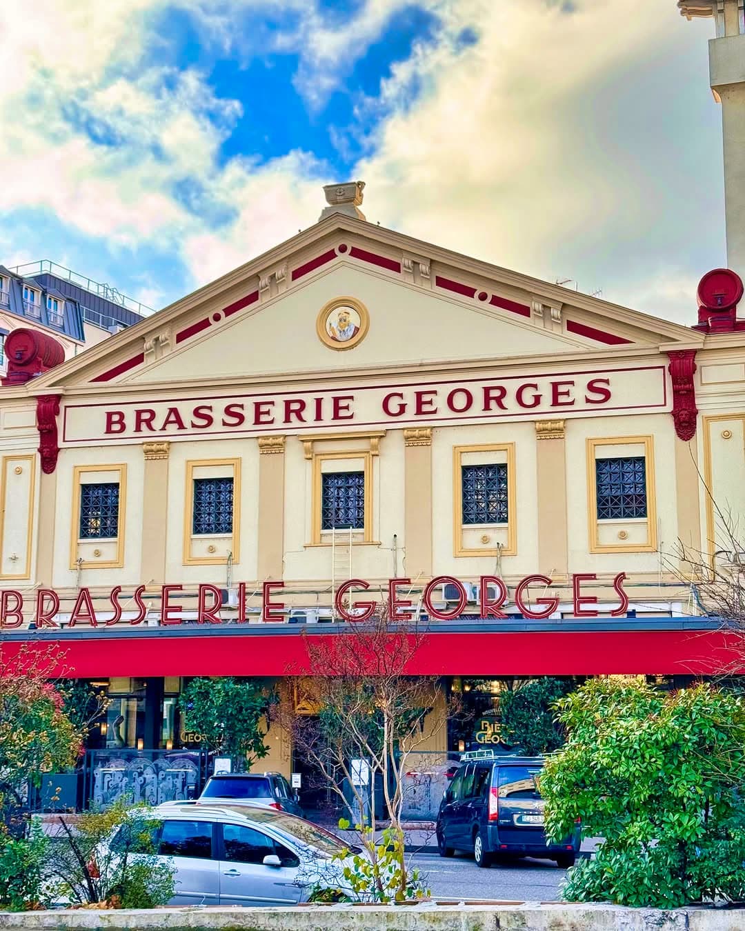 Façade jaune et rouge de la Brasserie Georges avec enseignes, ciel bleu nuageux