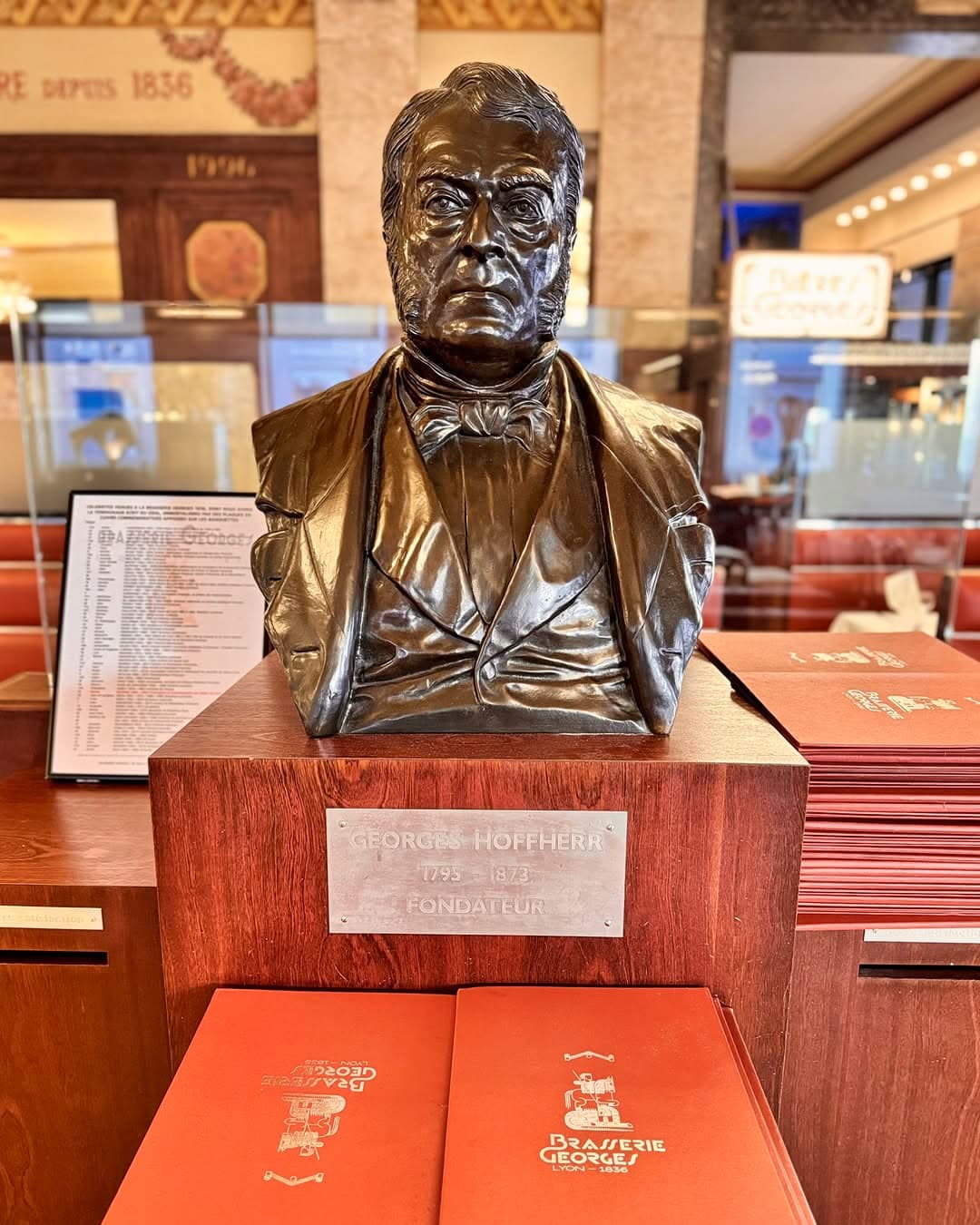 Buste en bronze du fondateur Georges Hoffherr sur socle avec plaque, salle en fond — Brasserie Georges