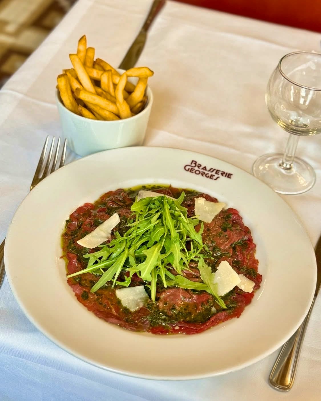 Un tartare de bœuf charolais et son pot de frites sur une assiette siglée Brasserie Georges, avec un verre