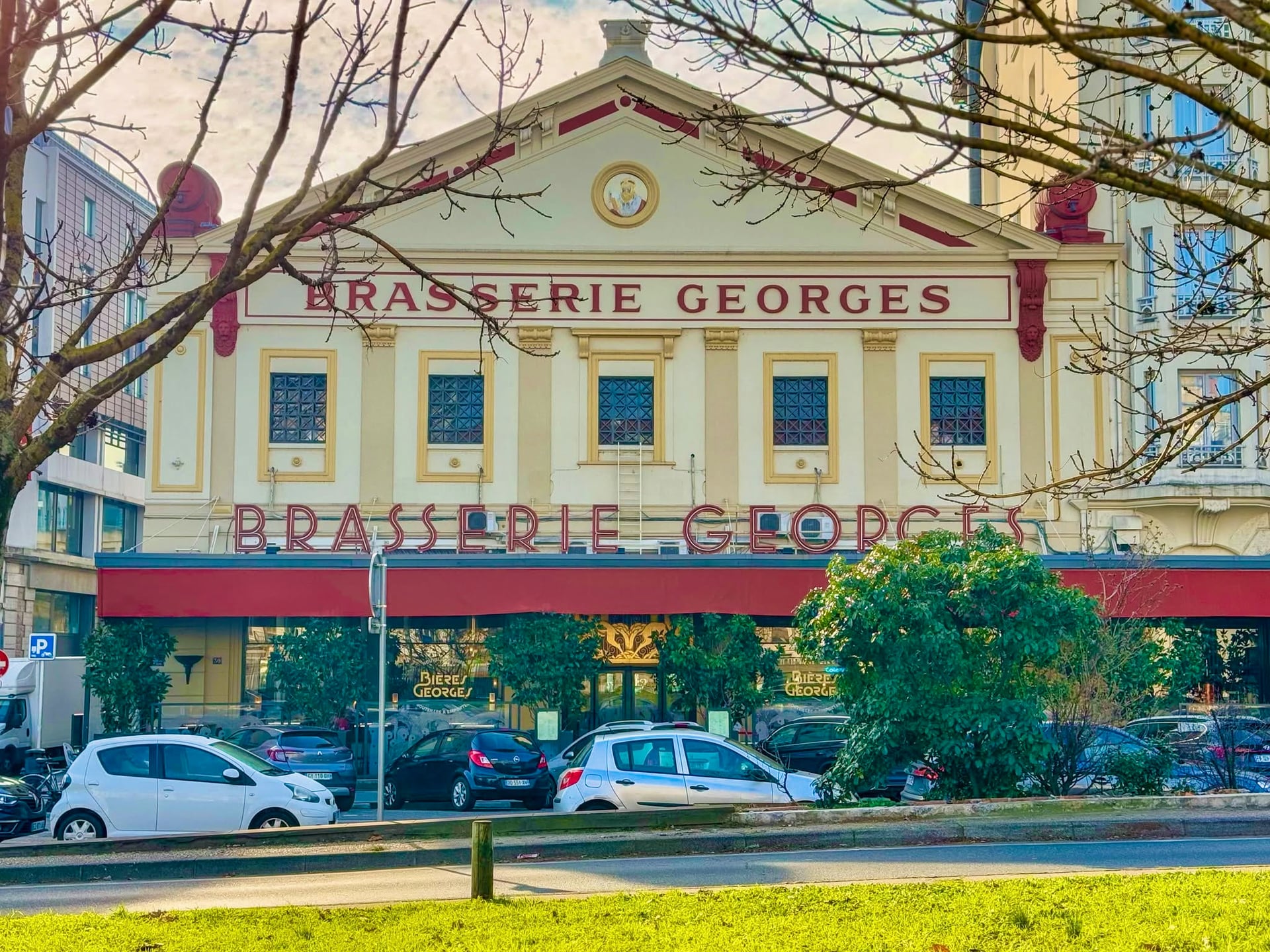 La façade de la Brasserie Georges de jour, son fronton et son enseigne rouge, vue depuis le cours de Verdun