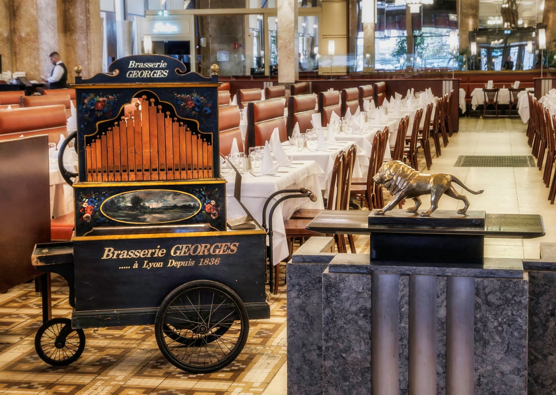 L'orgue de barbarie « Brasserie Georges à Lyon depuis 1836 » et le lion de bronze, devant les tables dressées de la grande salle