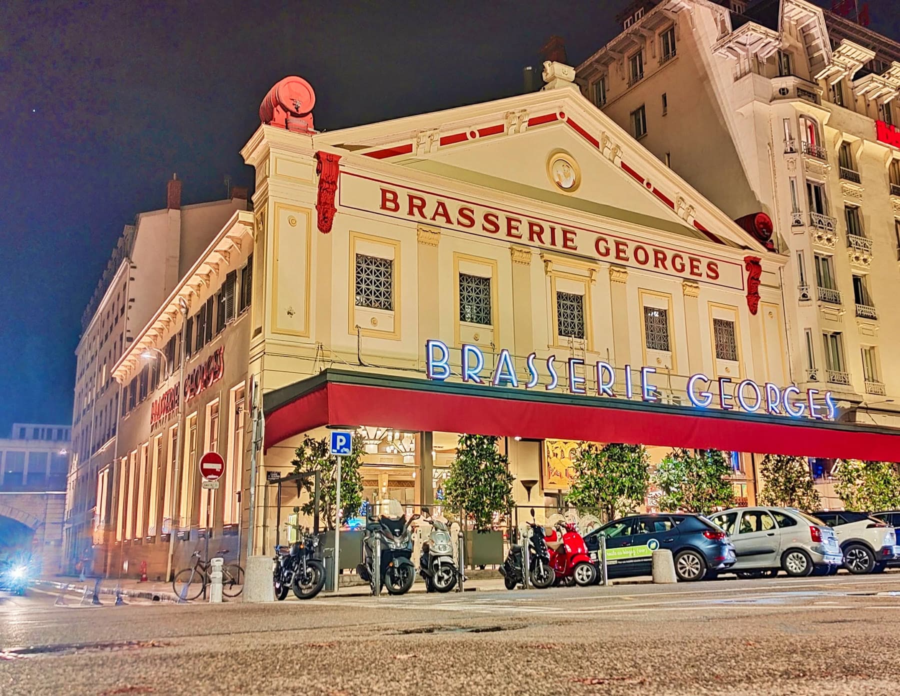 La façade illuminée de la Brasserie Georges vue depuis l'angle de la rue, à la nuit tombée