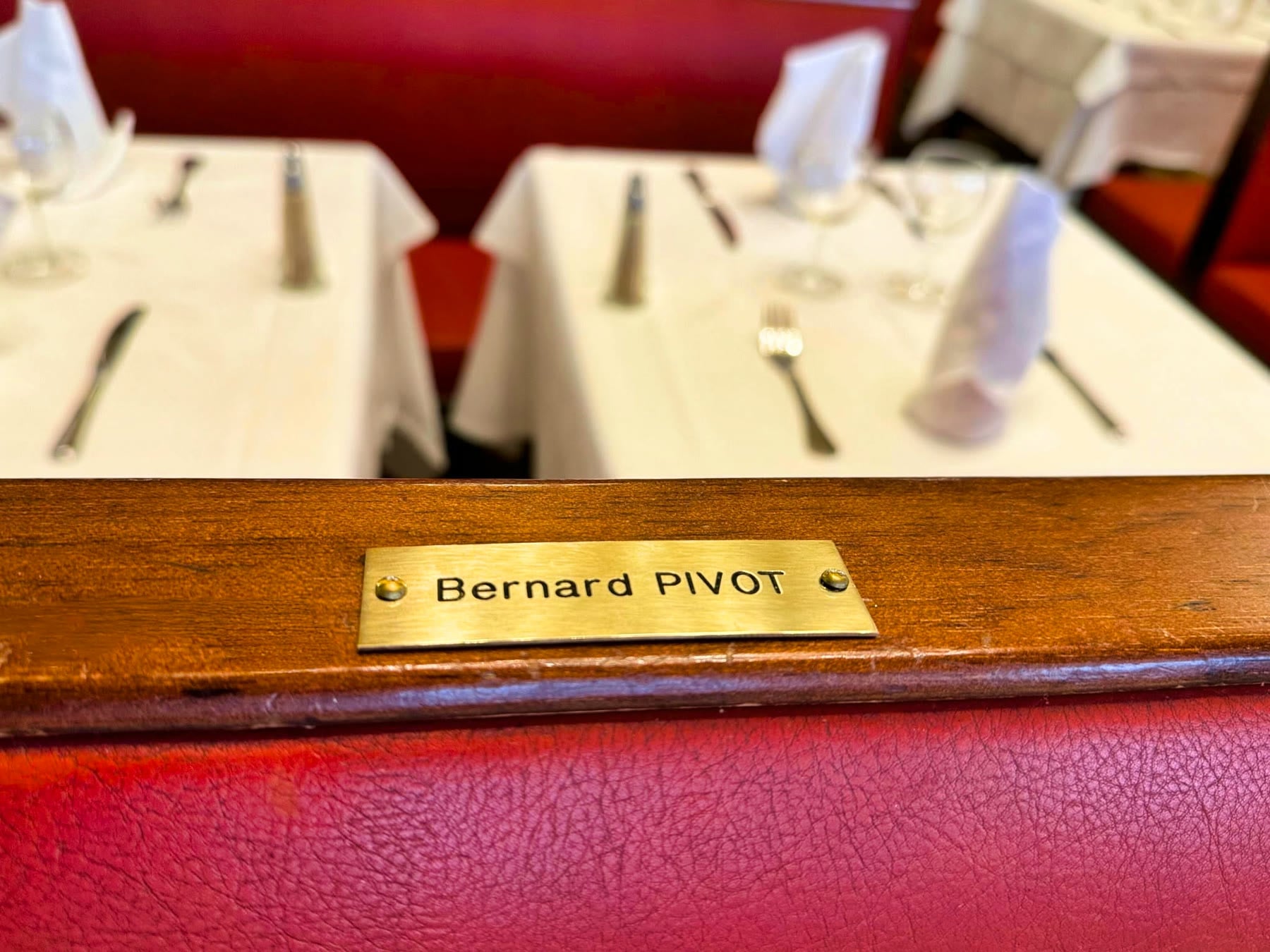 La plaque en laiton « Bernard PIVOT » vissée sur le dossier d'une banquette de la Brasserie Georges
